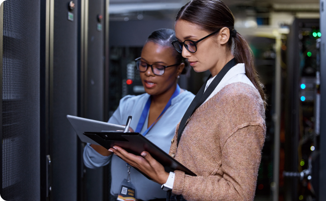two women looking at ipad and clipboard in a data server center